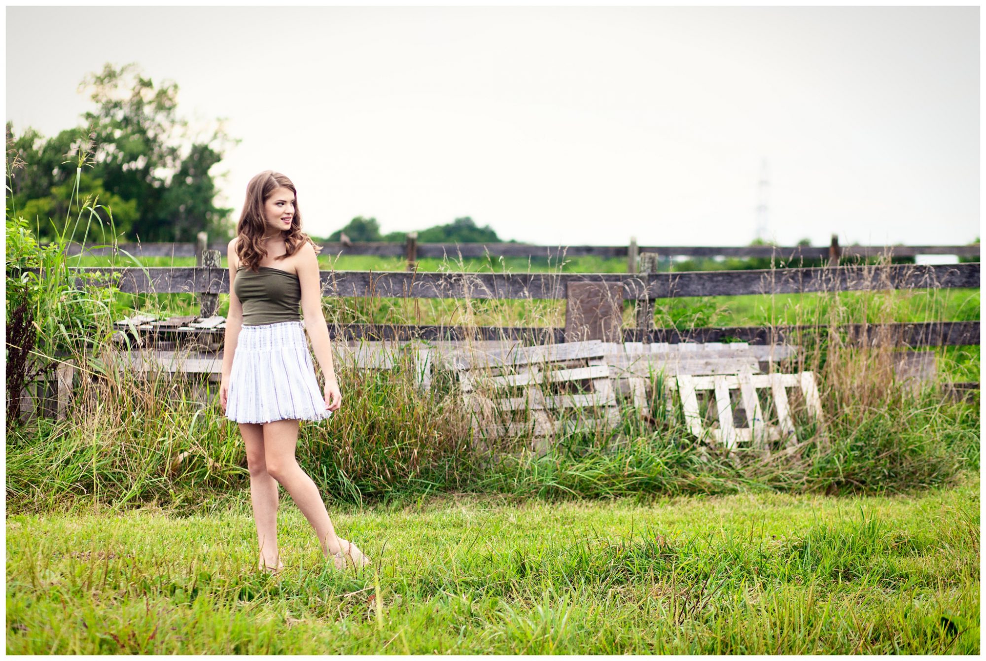 Senior girl in green shirt white skirt standing in open field