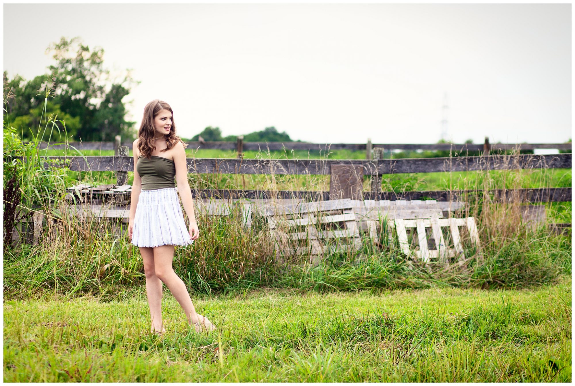Senior girl in green shirt white skirt standing in open field