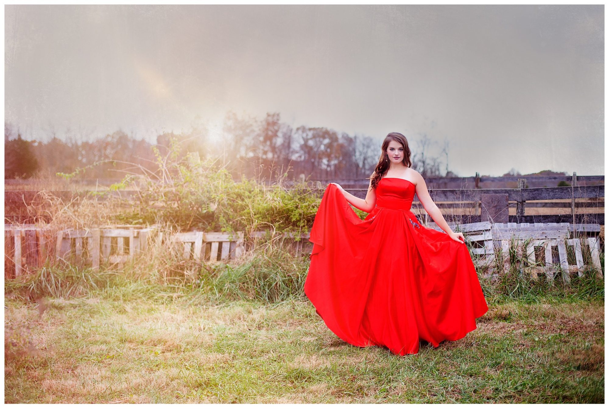 High school senior girl in red prom dress standing in beautiful field